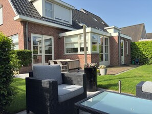 Ein Wohnhaus mit Terrasse, Gartenmöbeln, einem Swimmingpool und einer Ziegel-Fassade.