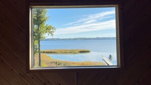 Ein Zimmer mit großem Fenster und Blick auf einen See, mit Holzwänden und einem Deckenventilator.