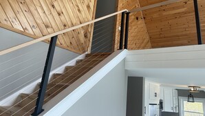 Eine Holztreppe mit Handlauf, einer Deckenleuchte und Blick auf einen Küchenbereich mit Schränken und einem Fenster.