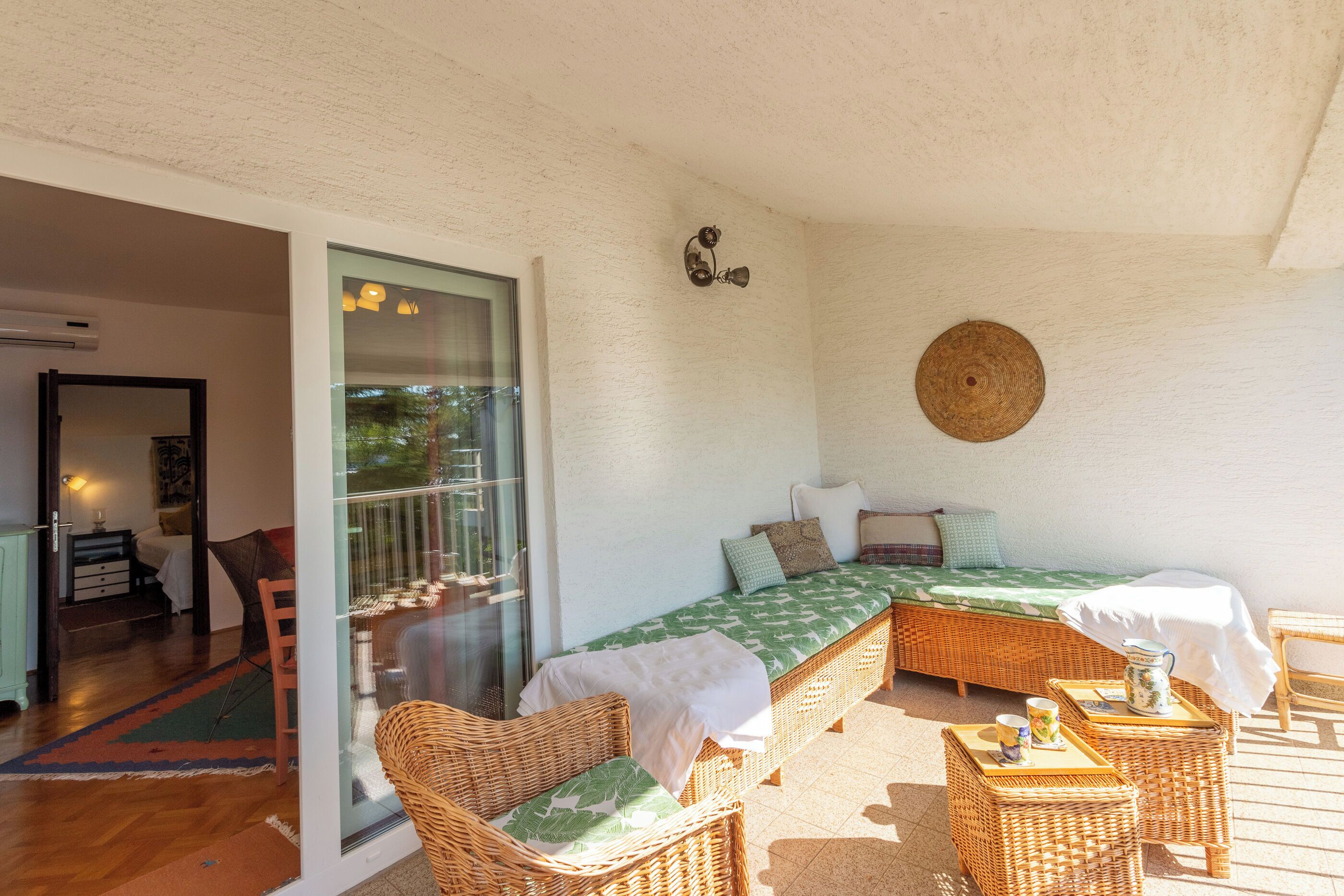 Habitación con cama, mobiliario de mimbre, ventilador de techo y vistas a través de un ventanal.