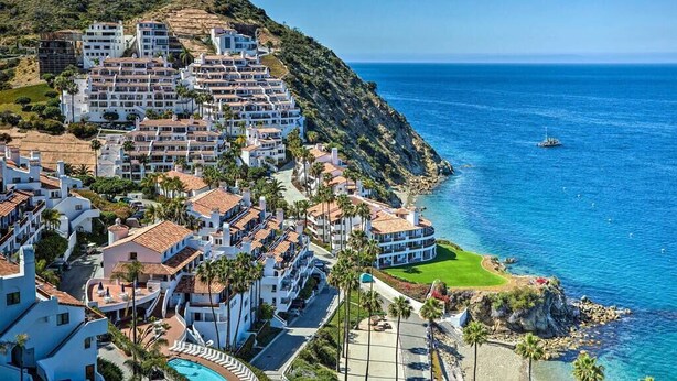A coastal resort with multiple white buildings, a pool, and a view of the sea.