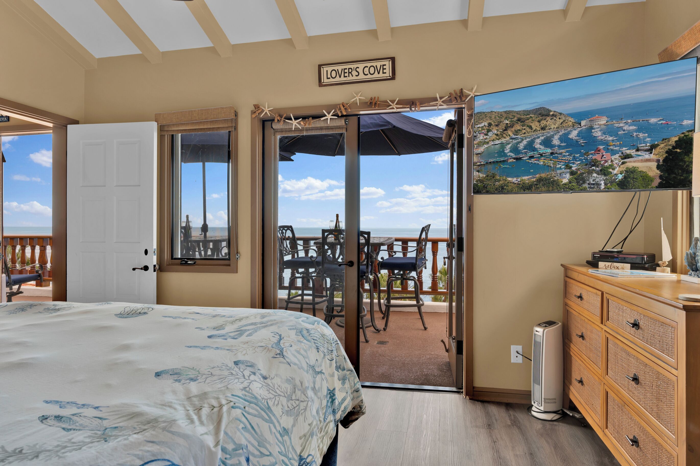 A bedroom with a bed, a dresser, and a TV displaying a coastal view.
