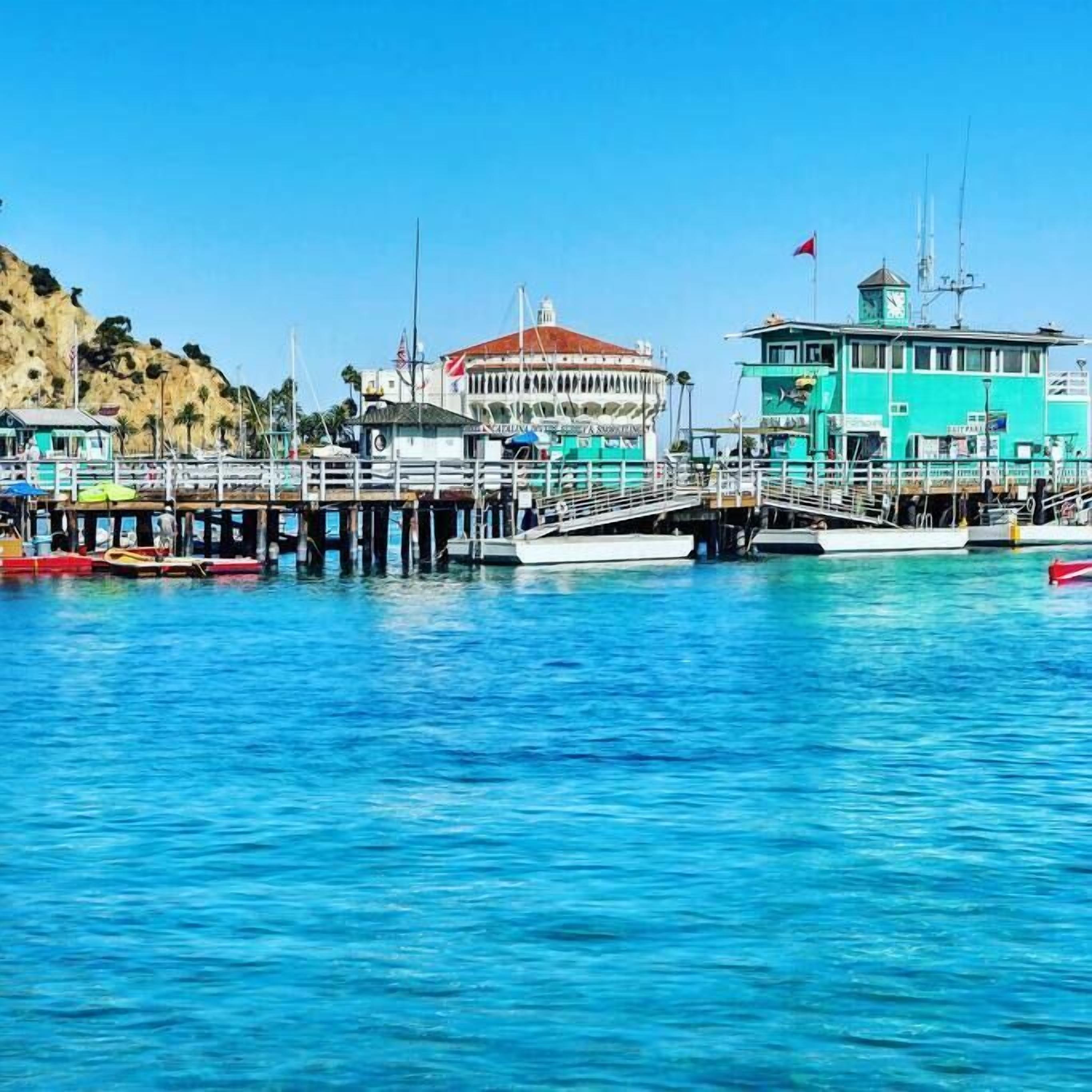 A pier with boats docked, a building with a red roof, and a turquoise structure with a flag.