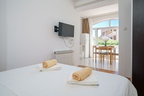A hotel room with two beds, a TV mounted on the wall, a radiator, and a view of the outside balcony.