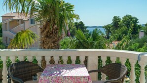 Un balcon avec une table et des chaises, offrant une vue sur la côte, avec des palmiers et des bâtiments.