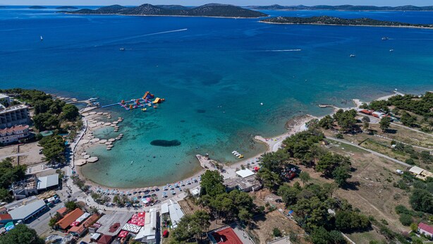 Vue aérienne d’une zone côtière avec des eaux cristallines, une plage et un petit port de plaisance.
