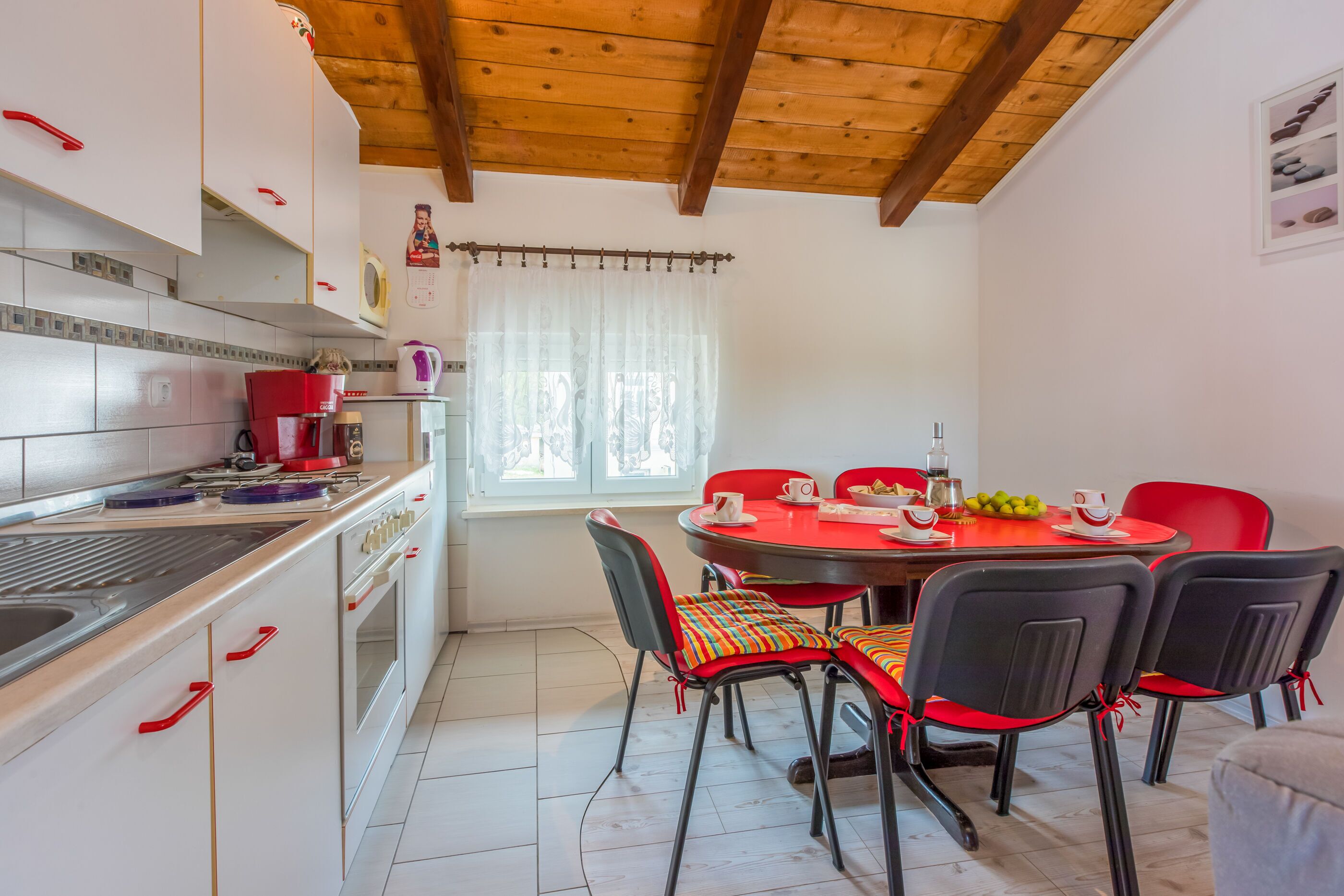 A kitchen with white cabinets, a wooden ceiling, and a dining area with a red table and chairs.