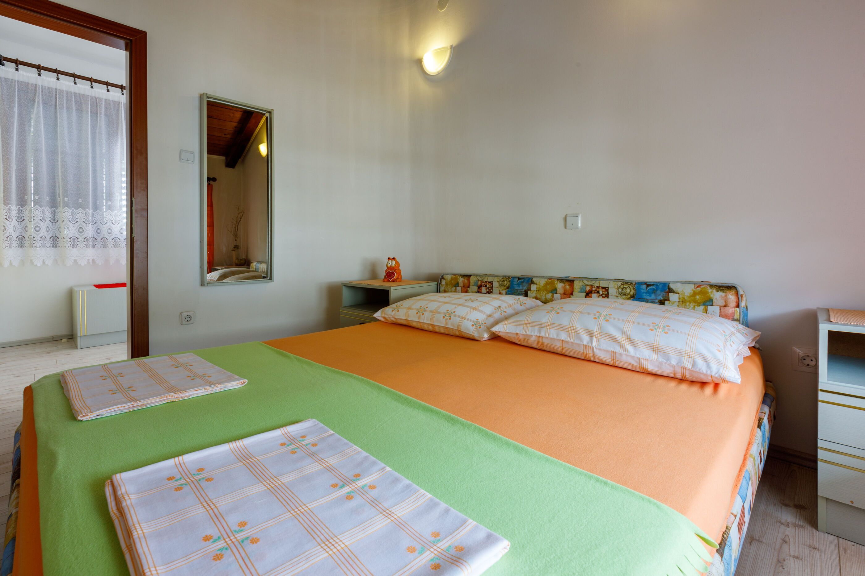 A bedroom with a bed, a nightstand, a mirror, and a window with curtains.