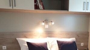 A neatly made bed with a dark blanket, a book on it, and a bedside table with a plant. - Mobile Home Pecten Exclusive 1 (Pakostane)