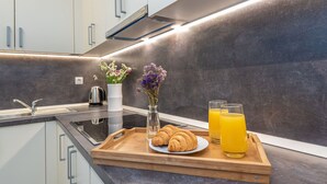 A modern kitchen with white cabinets, a dark backsplash, a stainless steel kettle, a vase with flowers, a tray with croissants and orange juice. - Mobile Home Pecten Exclusive 1 (Pakostane)