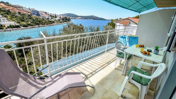 A balcony with a view of the sea, white chairs, a table with breakfast items, and a blue umbrella. - Apartment Seafront Apartments (Kalebova luka)