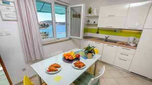 A modern kitchen with white cabinets, a dining table with chairs, a view of the sea, and a window with curtains. - Apartment Seafront Apartments (Kalebova luka)
