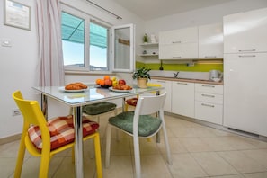 A modern kitchen with white cabinets, a glass table, and yellow chairs. - Apartment Seafront Apartments (Rogoznica)