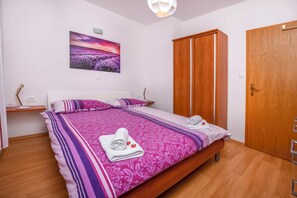 A bedroom with a large bed, wooden wardrobe, and a painting on the wall. - Apartment Seafront Apartments (Rogoznica)