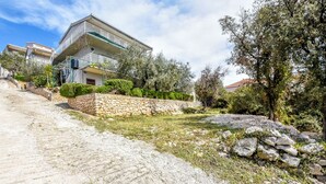 A residential building with a stone retaining wall, a paved driveway, and surrounding greenery. - Apartment Seafront Apartments (Kalebova luka)