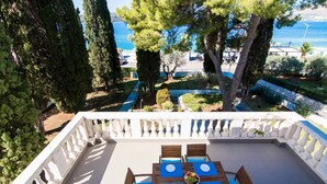 A terrace with a table set for four, overlooking a landscaped garden and a body of water. - Apartment Cypress (Okrug Gornji)
