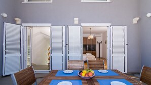 A dining area with a table set for two, a bowl of fruit, and a view into a bedroom. - Apartment Cypress (Okrug Gornji)