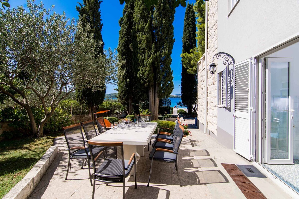 Un espace de restauration en plein air, avec une table et des chaises, entouré d’arbres et bordé d’un bâtiment doté d’une porte en verre.