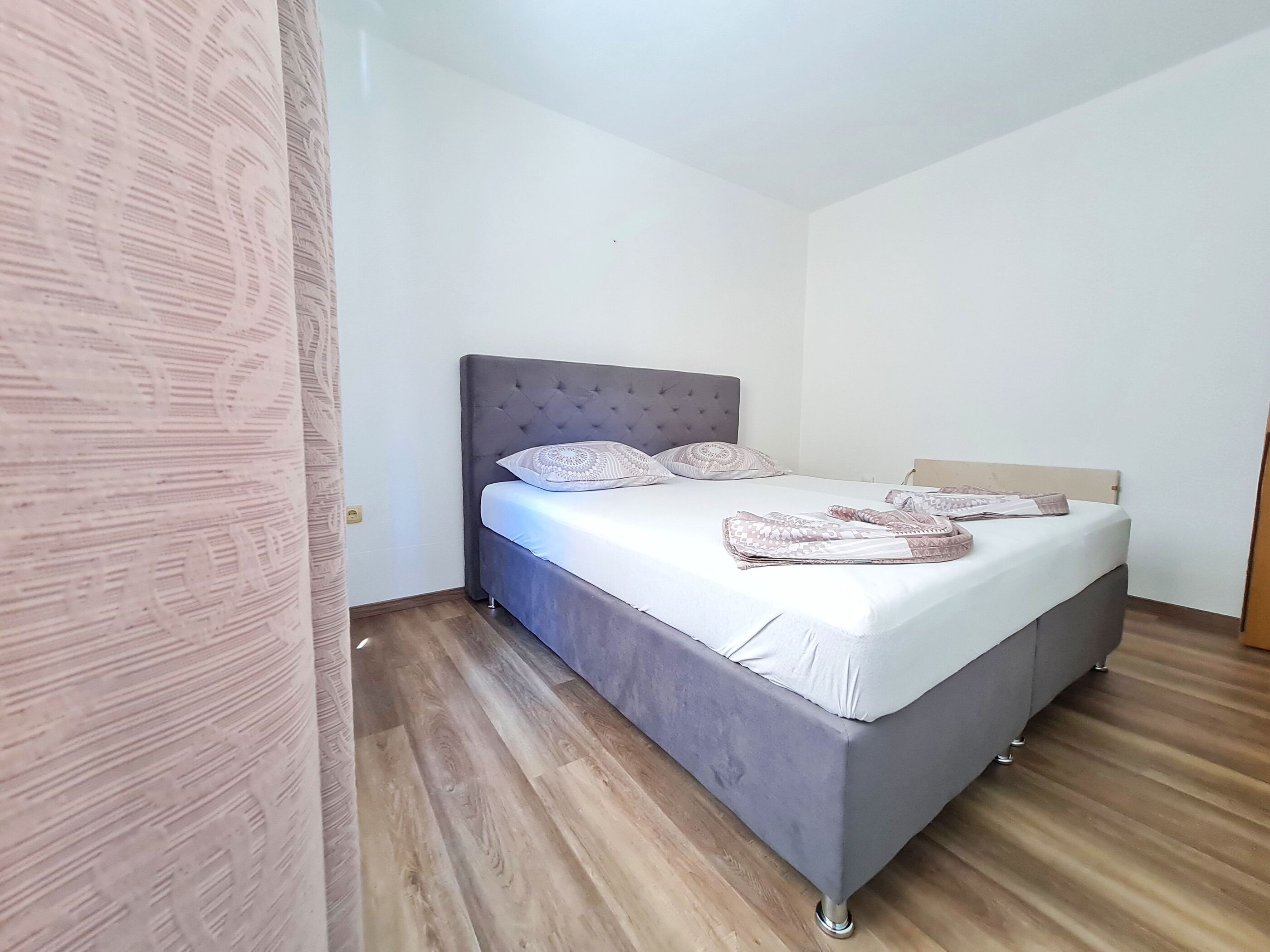 A single-bed room with a grey upholstered headboard, white bedding, and a patterned throw blanket.