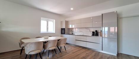A modern kitchen with white cabinets, a dining table with chairs, and a built-in oven.