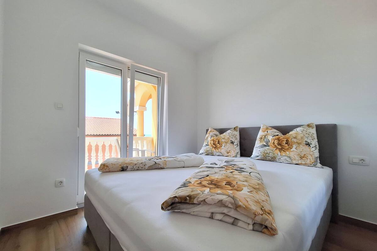 A bedroom with a bed, two pillows, a window, and a view of a balcony.