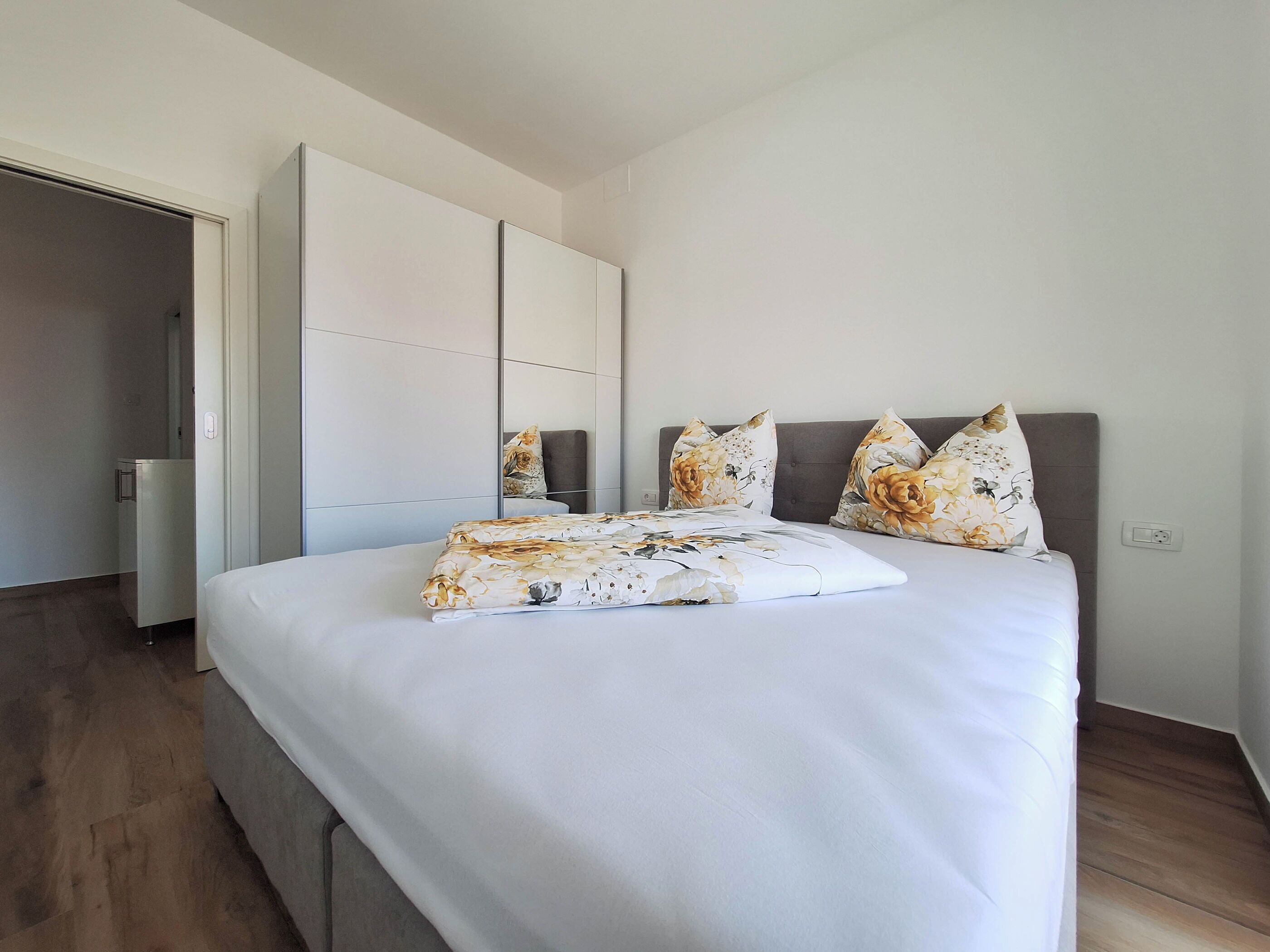 A modern bedroom with a large bed, a wardrobe, and a mirror.