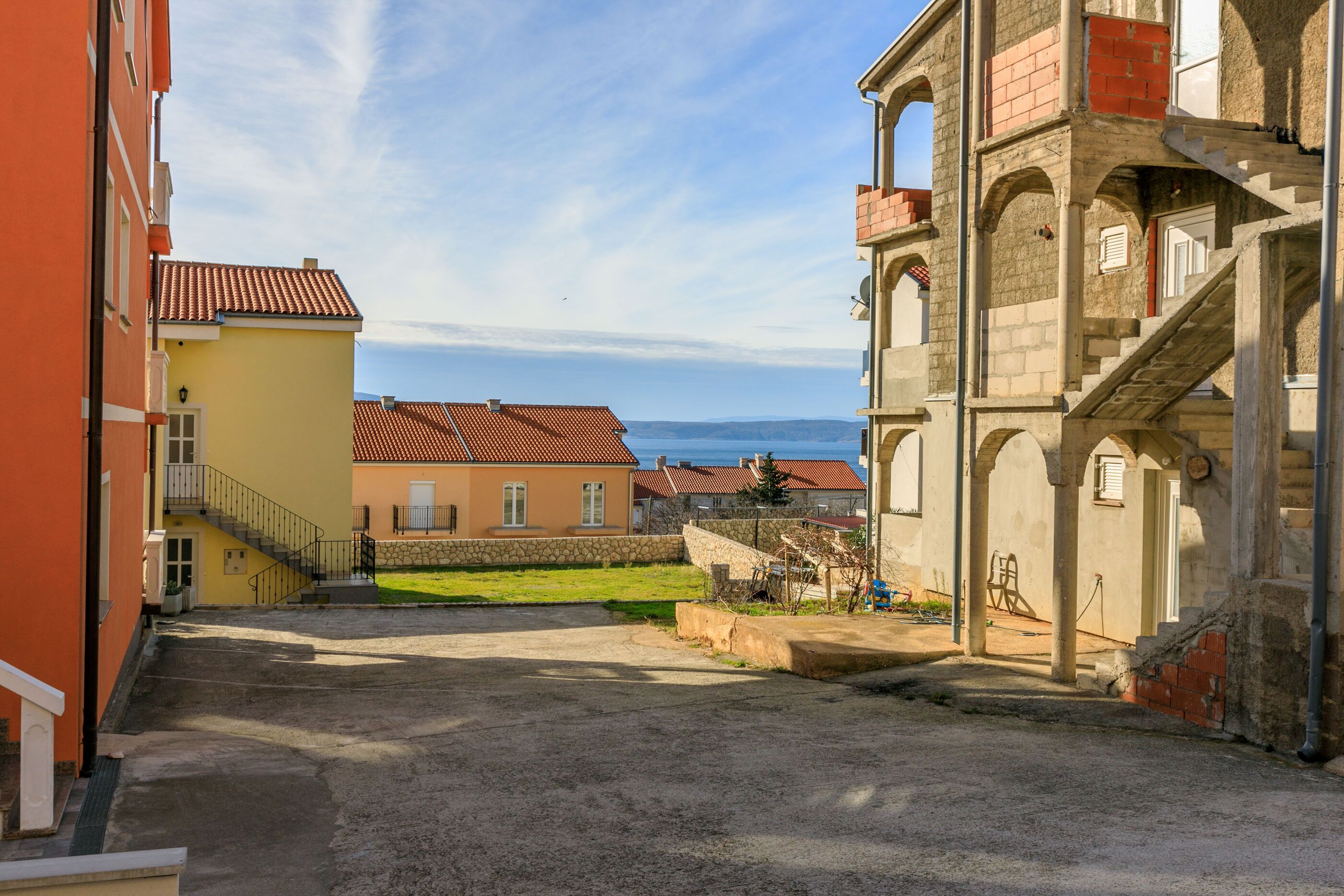 A narrow street with buildings on either side, a stone staircase, and a view of the sea in the distance.