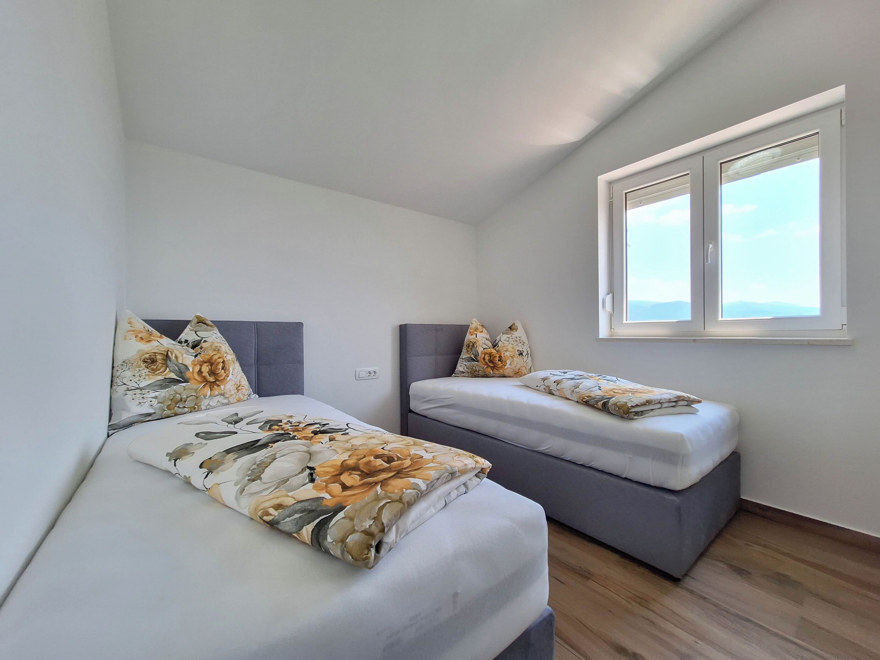 Une chambre à coucher avec deux lits, chacun agrémenté de draps à motifs floraux et de têtes de lit grises.