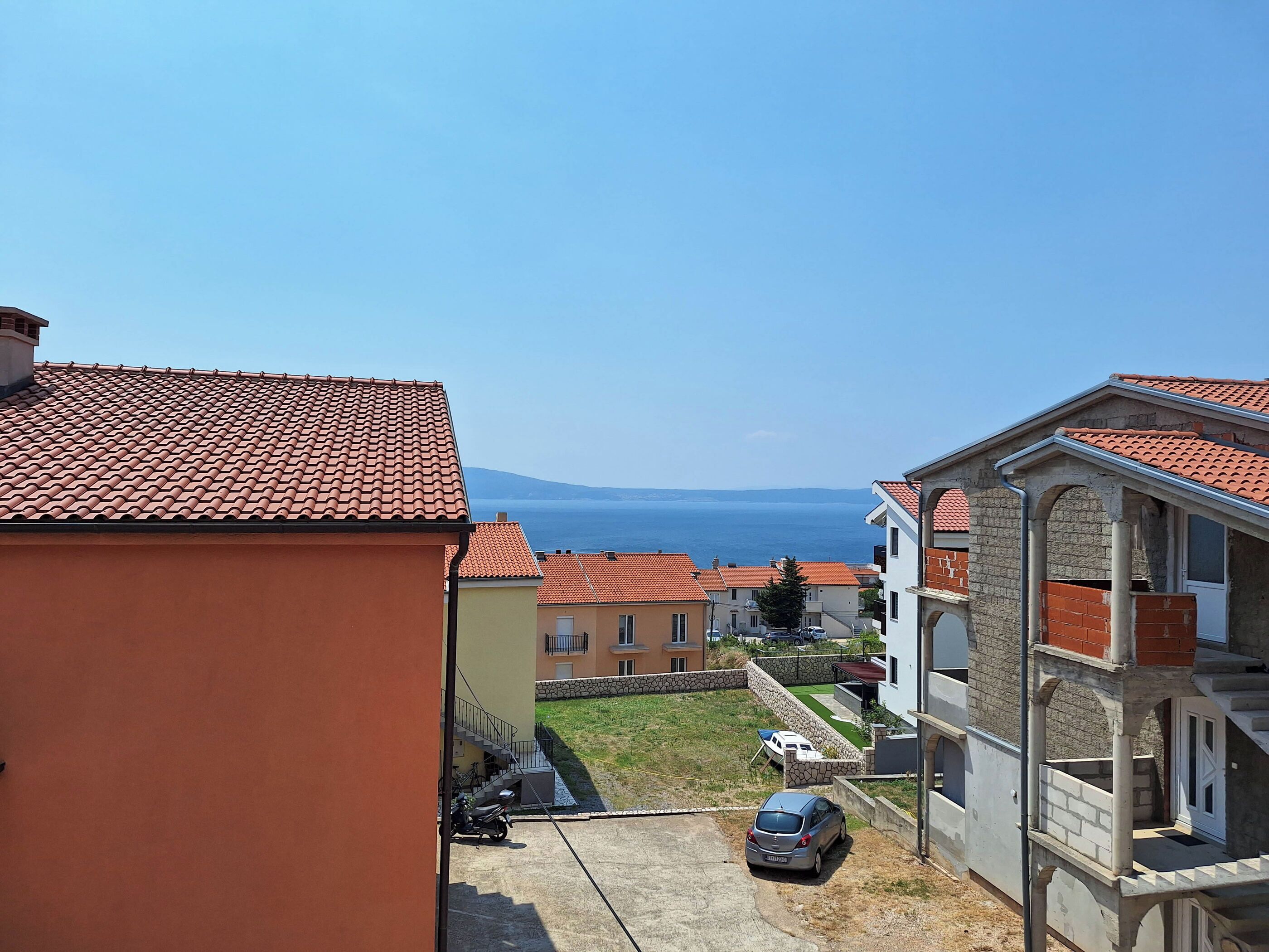 A residential area with terracotta tiled roofs, a clear view of the sea, and a mix of modern and traditional architecture.