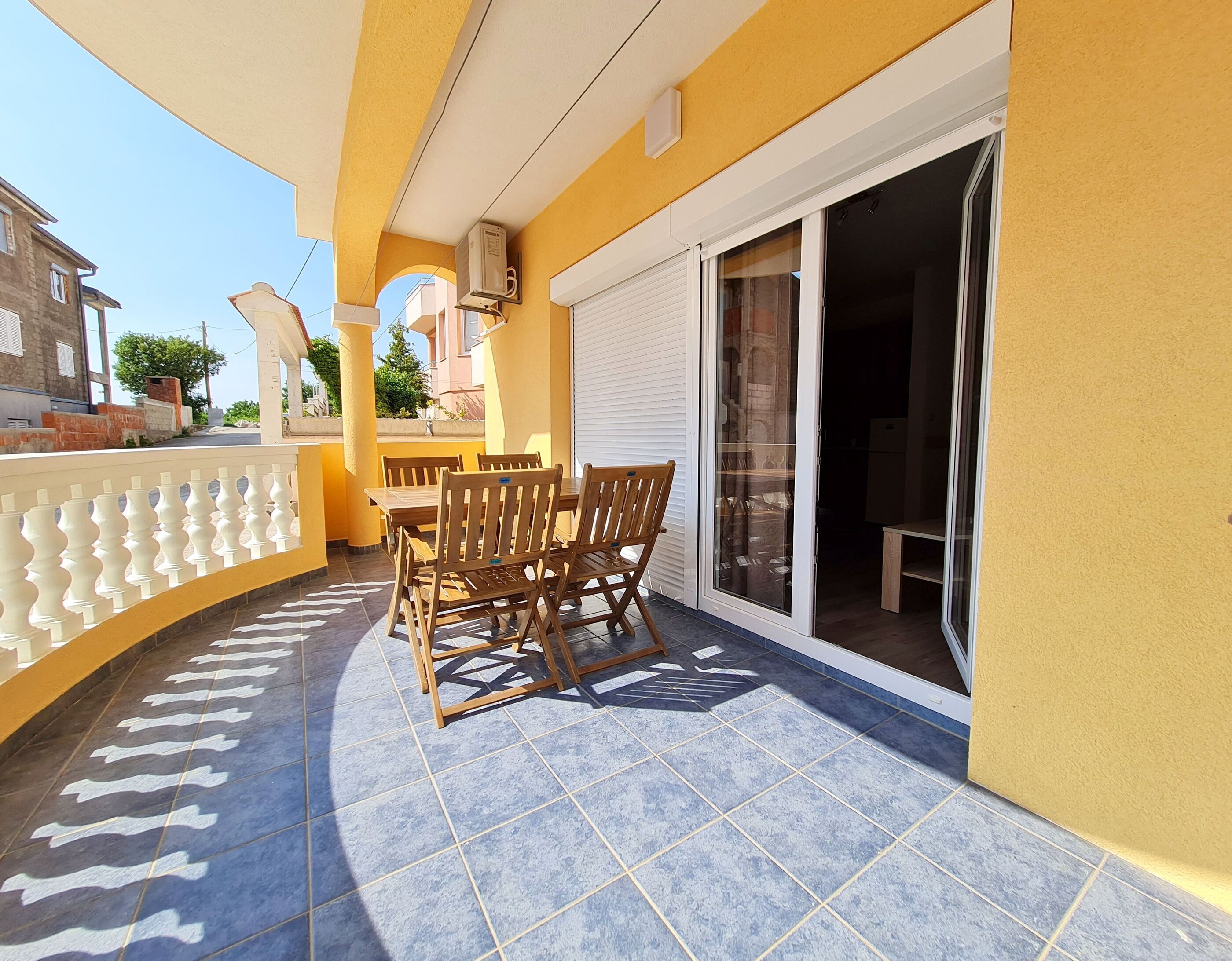 Un balcon avec une table et des chaises, une porte-fenêtre coulissante et un mur jaune.