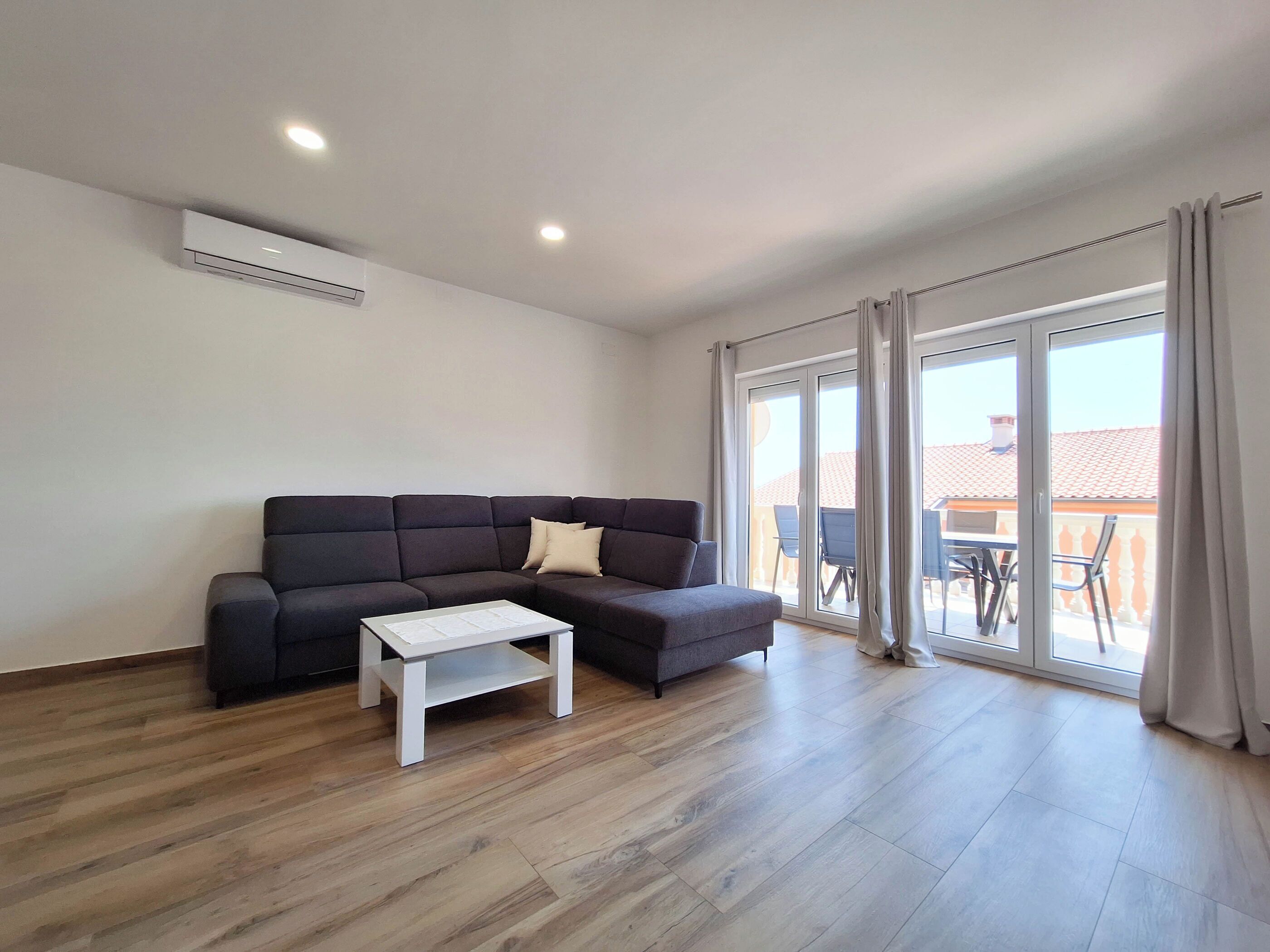 Een moderne woonkamer met een modulaire bank, een klein witte salontafel en een glazen schuifdeur die leidt naar een balkon.