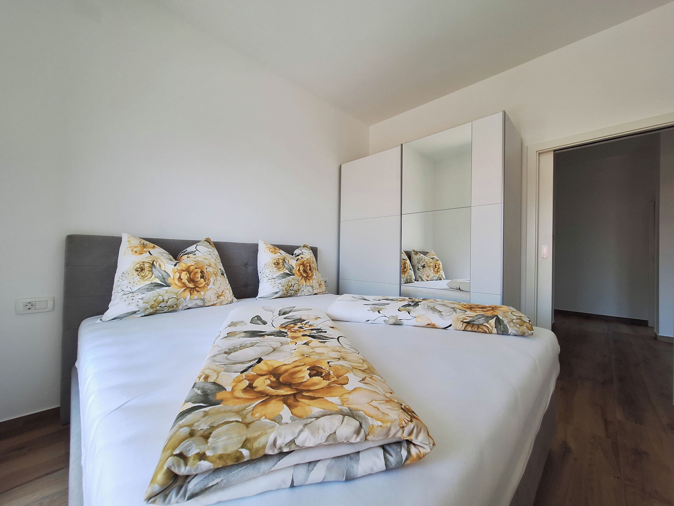 A bedroom with a large bed, a grey headboard, and a wardrobe with mirrored doors.