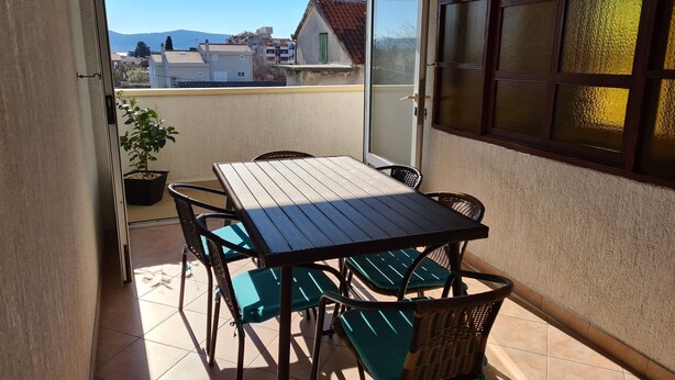 A balcony with a table and chairs, a potted plant, and a view of buildings and mountains. - Apartment Donna (Biograd)