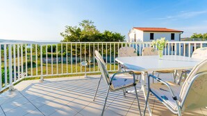 Una terrazza con tavolo e sedie bianche, un recinto bianco e vista su un edificio e vegetazione.
