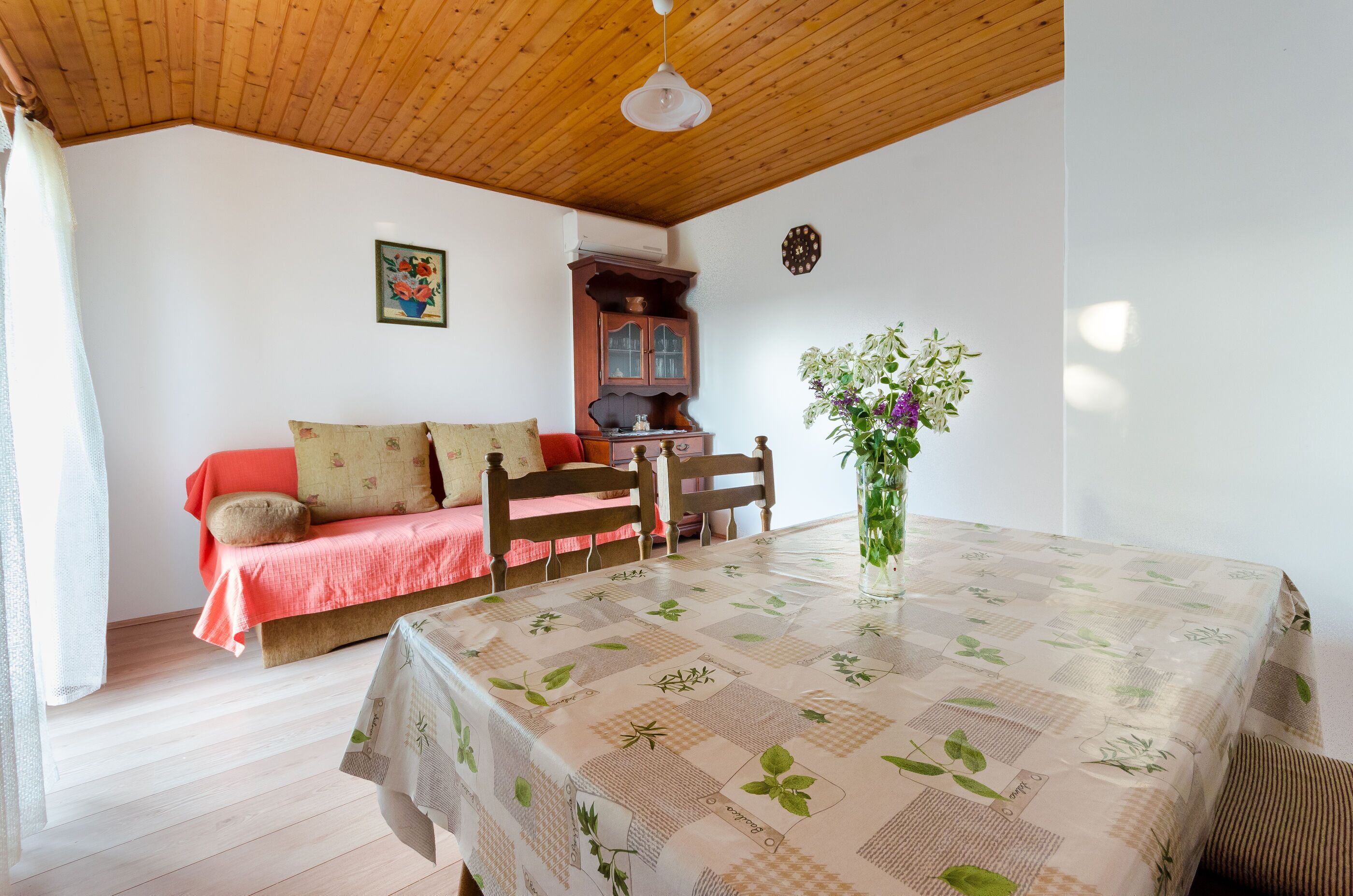 Una habitación acogedora con una mesa de comedor, un sofá, un armario y un reloj en la pared.
