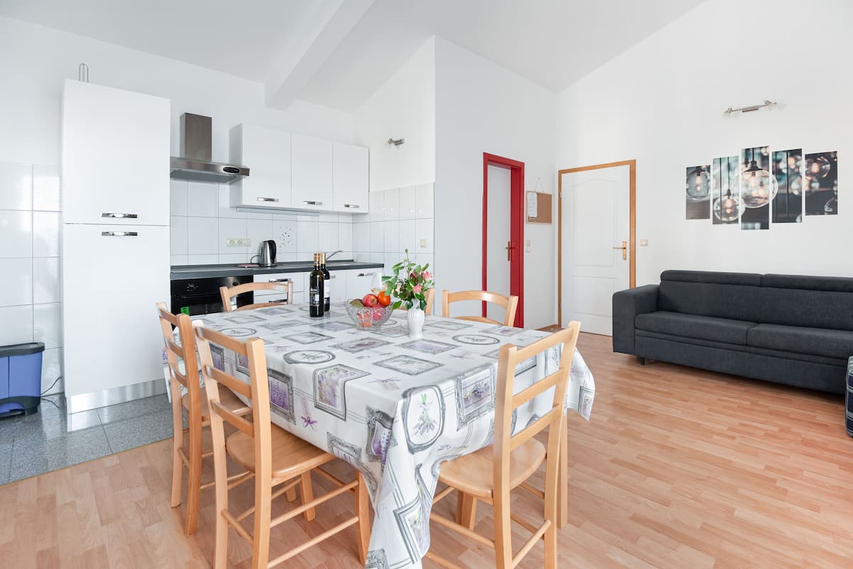 A modern kitchen with white cabinets, a dining table with a patterned tablecloth, and a gray sofa in the living area.