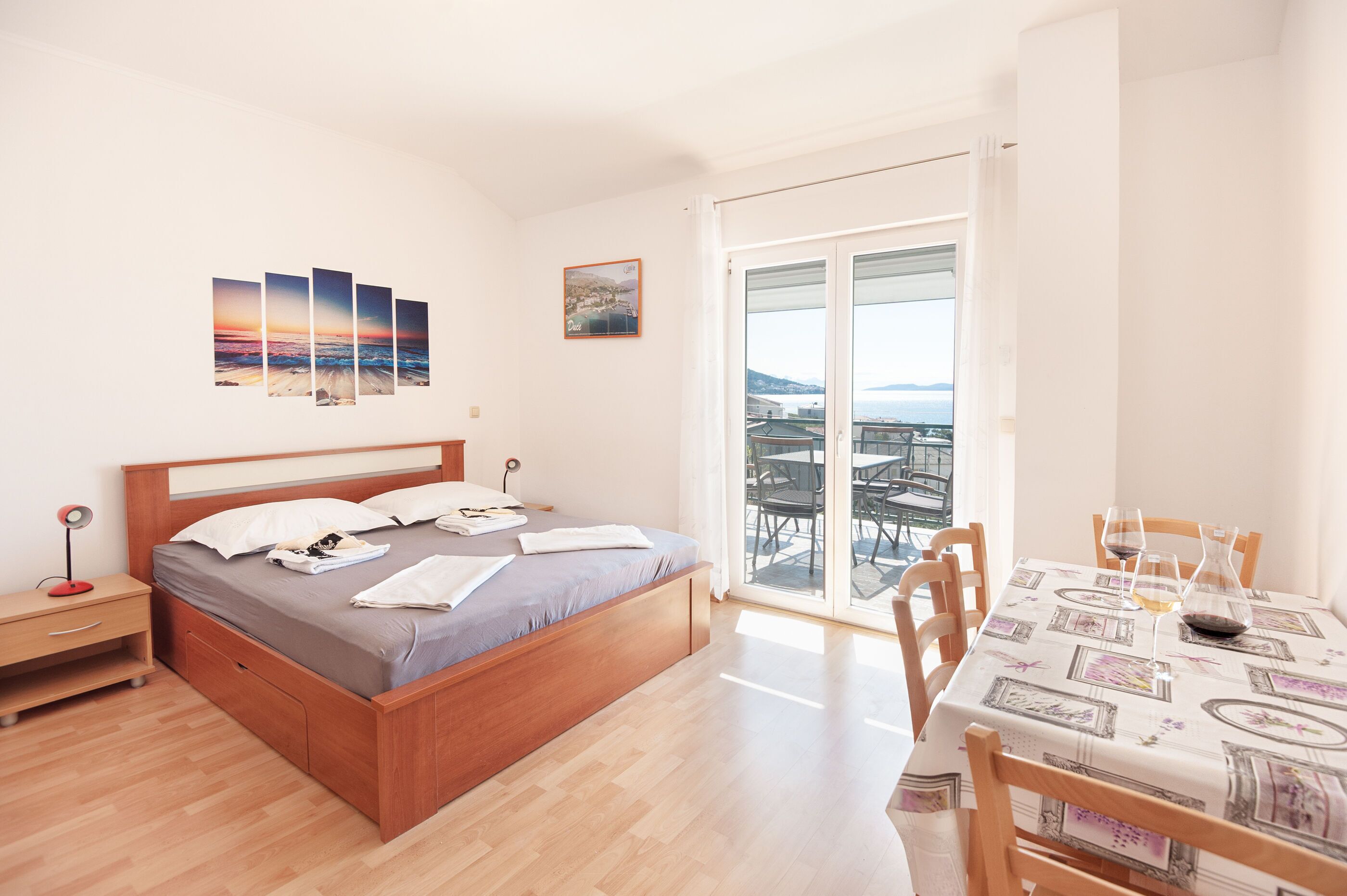 A bedroom with a bed, bedside table, and a view of the city through a balcony.