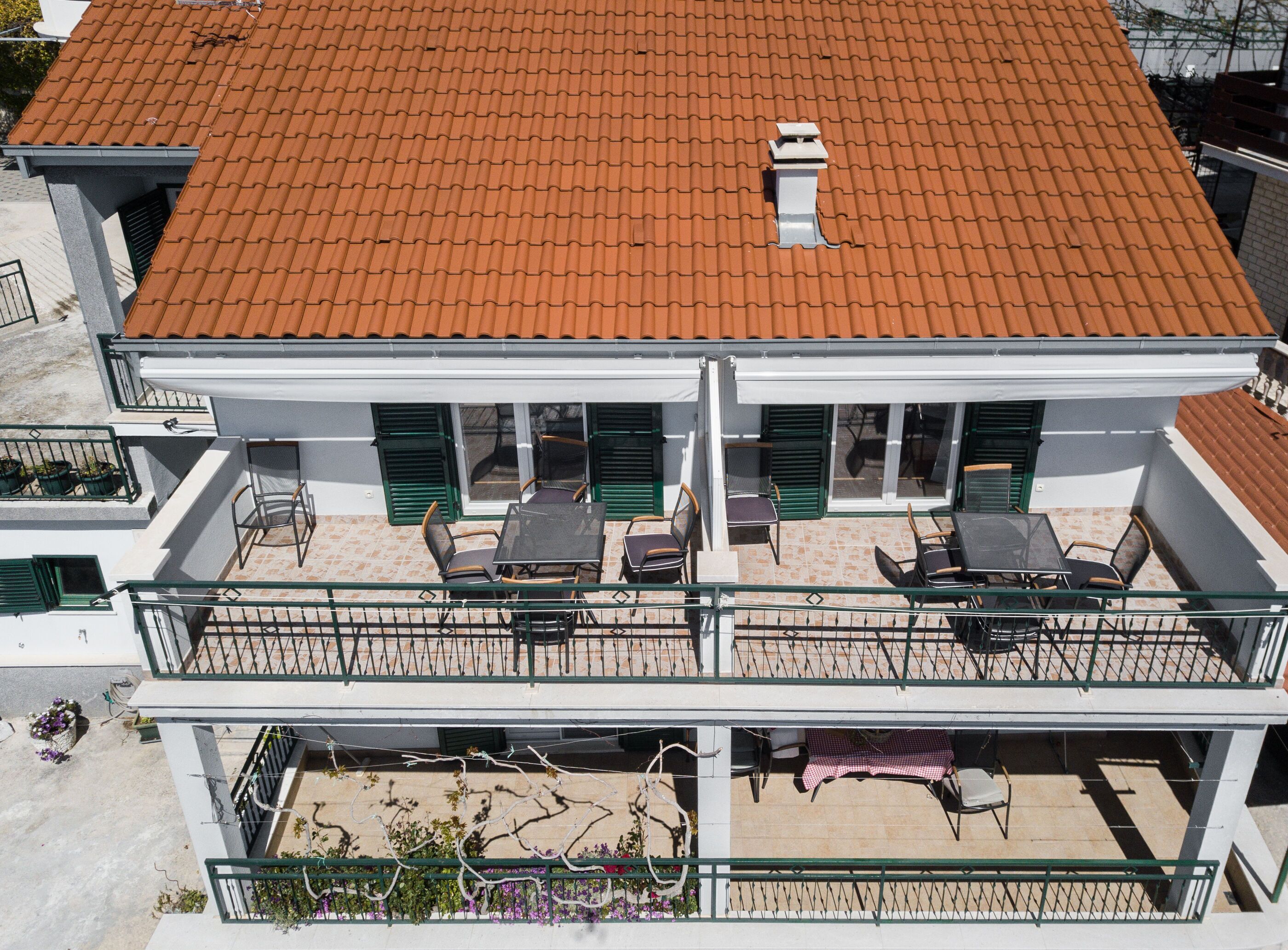 A two-story building with a red-tiled roof, a balcony with outdoor seating, and a white facade.