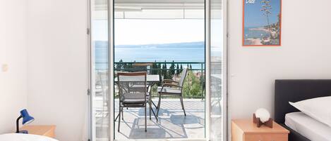 A bedroom with a bed, a nightstand, a bedside table, and a view of a balcony with outdoor furniture.