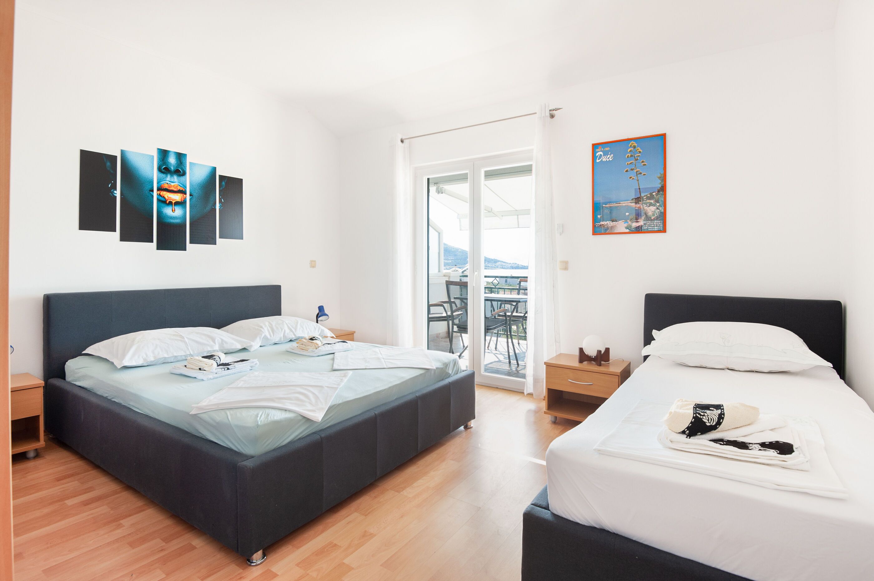 Een moderne hotelkamer met een groot bed, een kleiner bed, een balkon met uitzicht en kunstwerken aan de wanden.