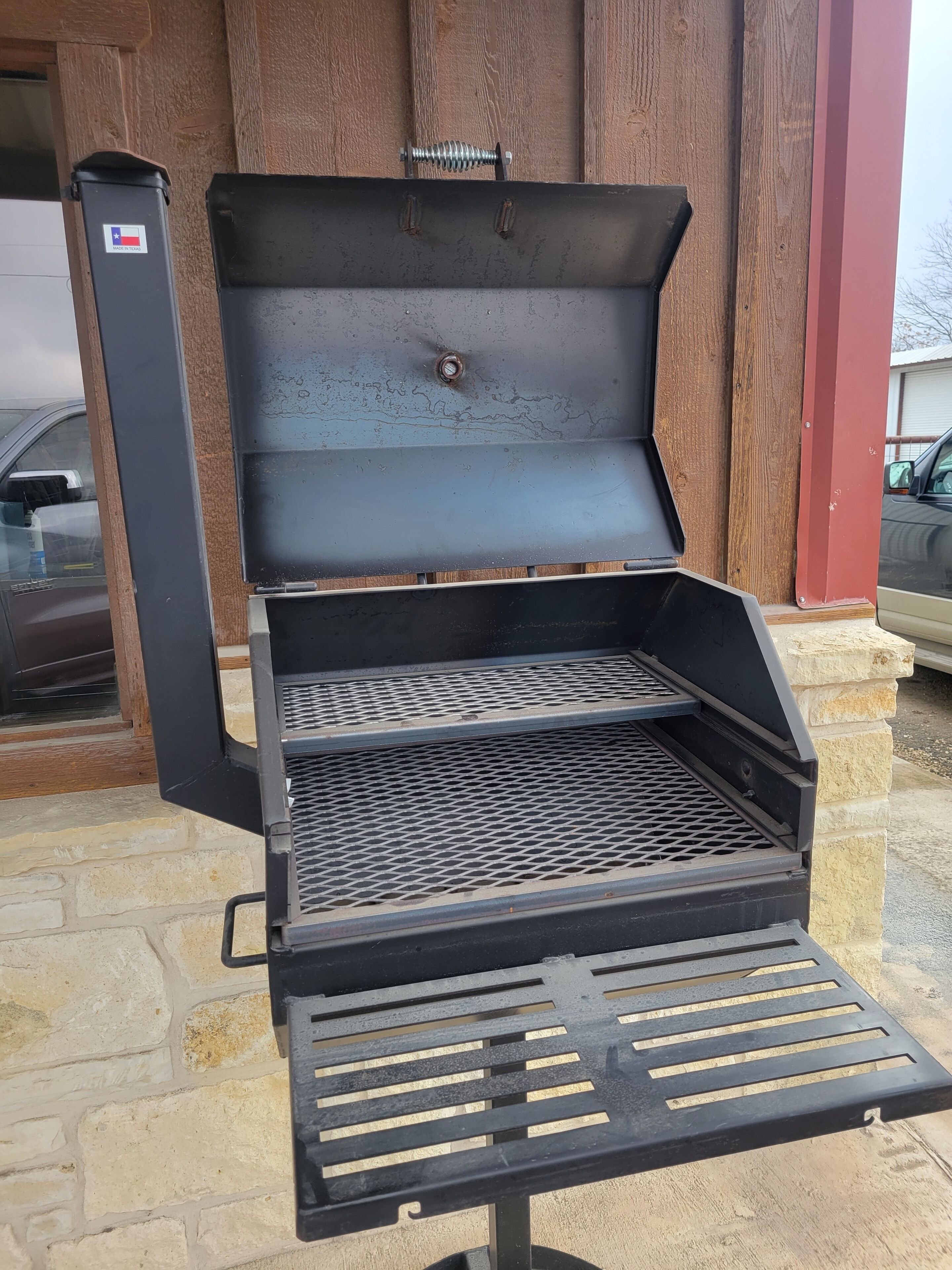 Ein Grill mit einem Metallrost, einem Klappdeckel und einem Metallgriff.