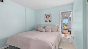 A bedroom with a bed, a window, and a small table with a lamp.