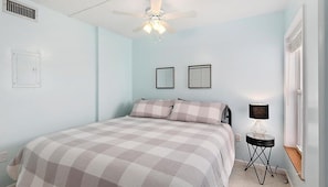 Een slaapkamer met een bed, een plafondventilator, een wandlamp en een raam.