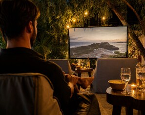A person seated on a couch facing a television displaying a scenic view of a coastline.