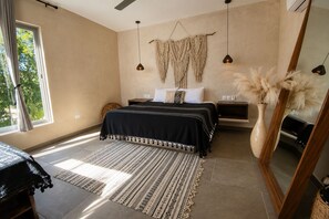 A bedroom with a bed, bedside tables, a mirror, a window, and a decorative macrame wall hanging.