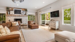 Amplia sala de estar con chimenea de ladrillo, un televisor grande y un balcón con mobiliario exterior.