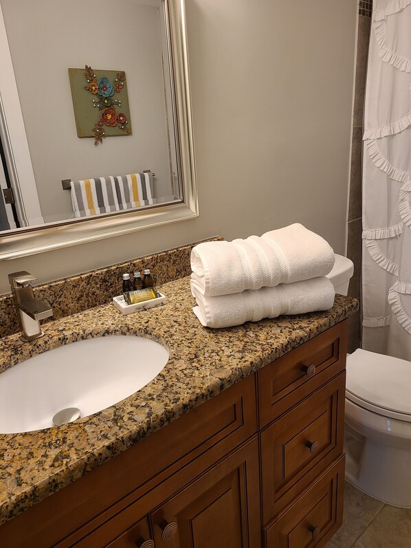 A bathroom with a granite countertop, a white sink, a mirror, a towel rack, and a toilet.