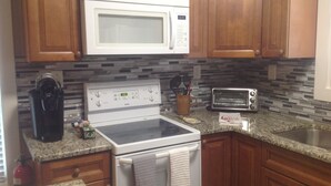 A kitchen with wooden cabinets, a white stove, a microwave, a toaster, and a coffee maker. - Water Feature Cottage (Raleigh)