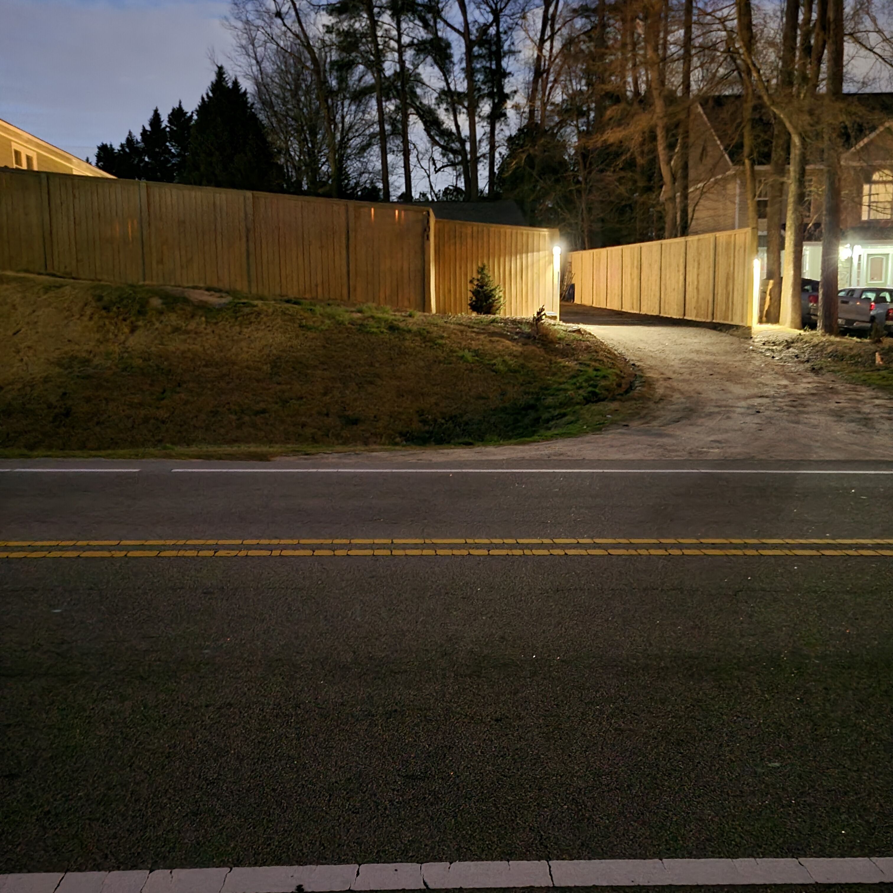 A paved road with a wooden fence and a building in the background.