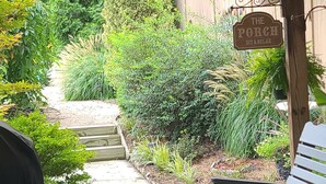 A covered patio area with outdoor seating, a pathway leading to a wooden deck, and a sign reading "The Porch Sit & Relax". - Water Feature Cottage (Raleigh)